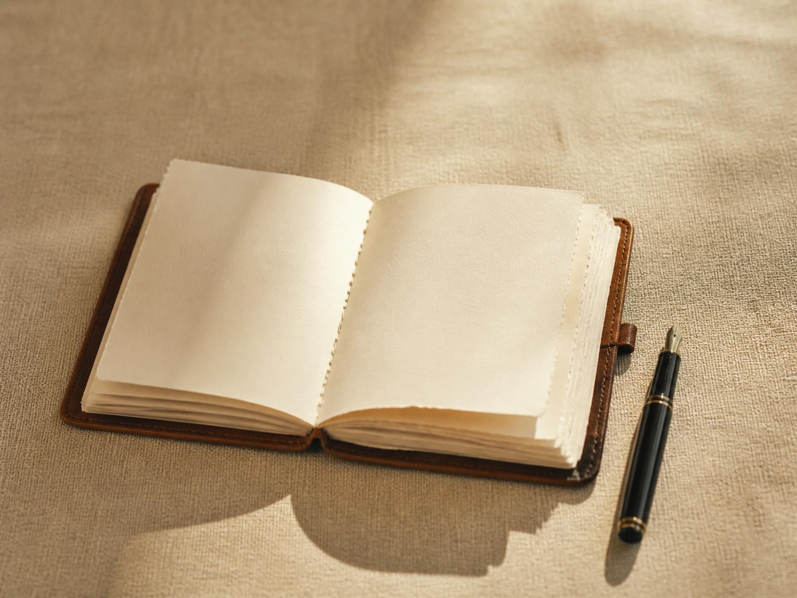 Caderno de couro aberto sobre linho, com caneta ao lado, luz matinal suave